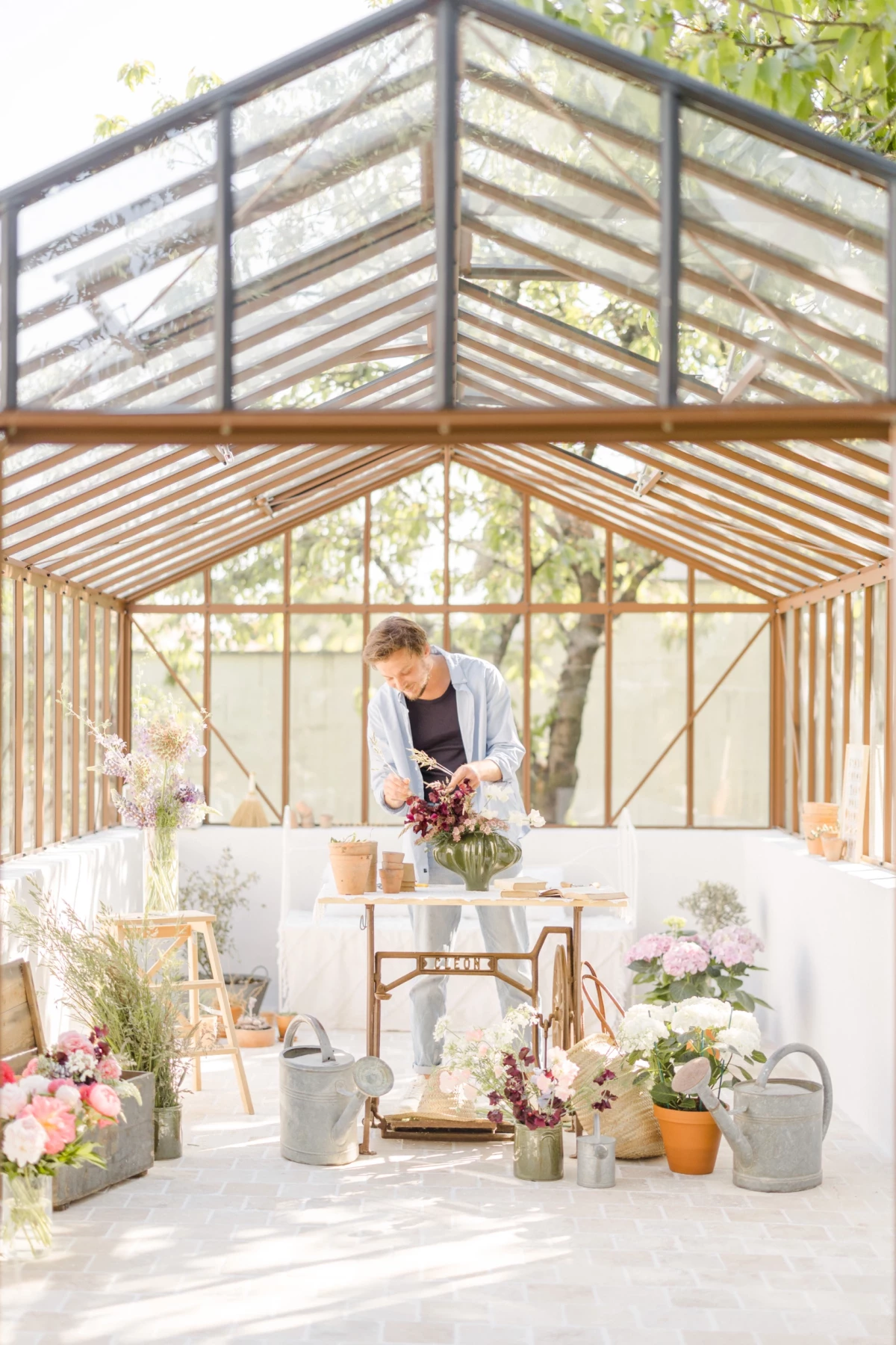 Portrait professionnel d'une fleuriste arrangeant des fleurs dans sa verrière lumineuse, ambiance douce et naturelle en Vendée