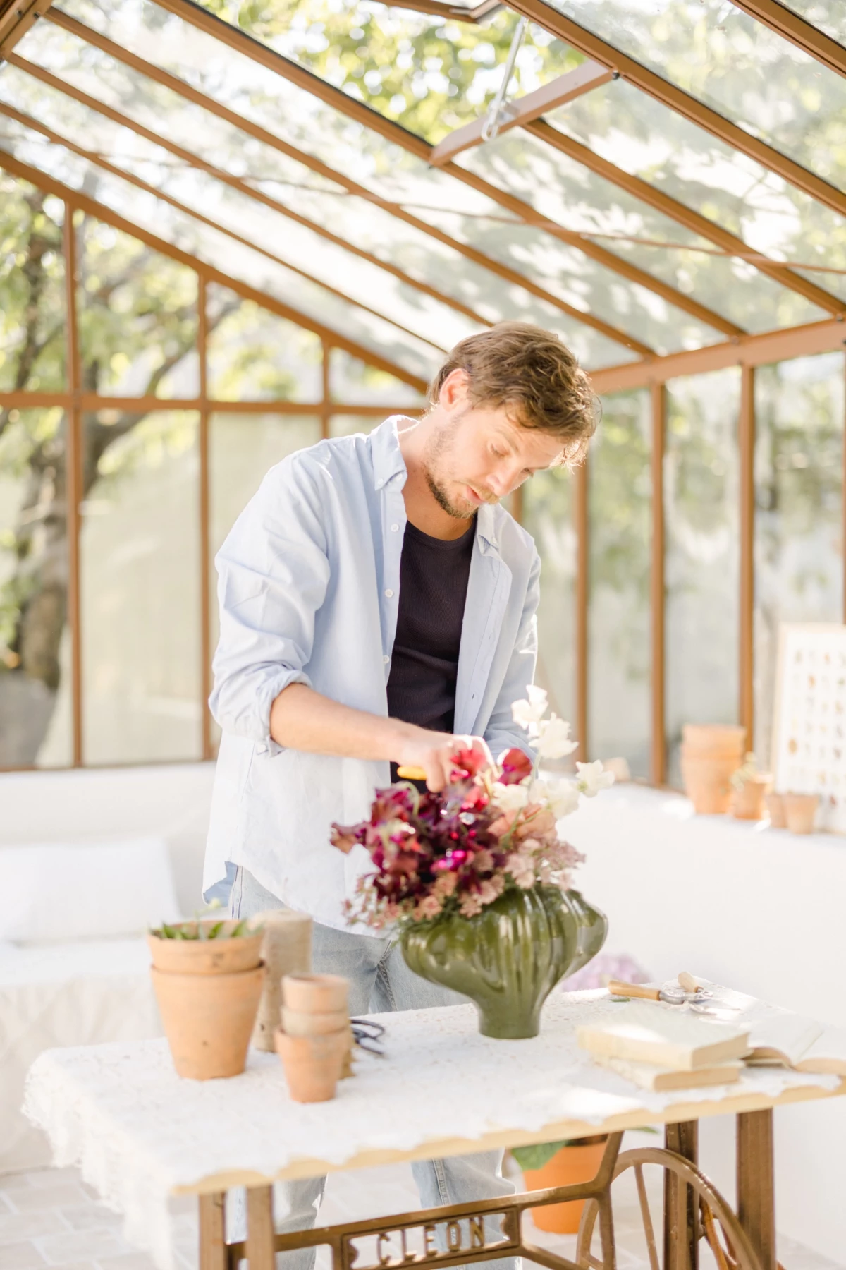 Portrait corporate fleuriste : artisan créant un bouquet de fleurs sous verrière lumineuse, ambiance douce et naturelle en Vendée