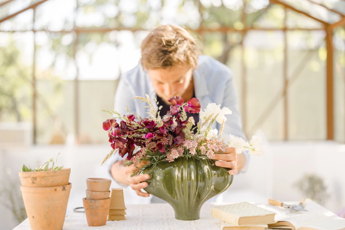 Portrait corporate fleuriste Vendée : artisan compose un bouquet dans une verrière lumineuse, ambiance douce et naturelle