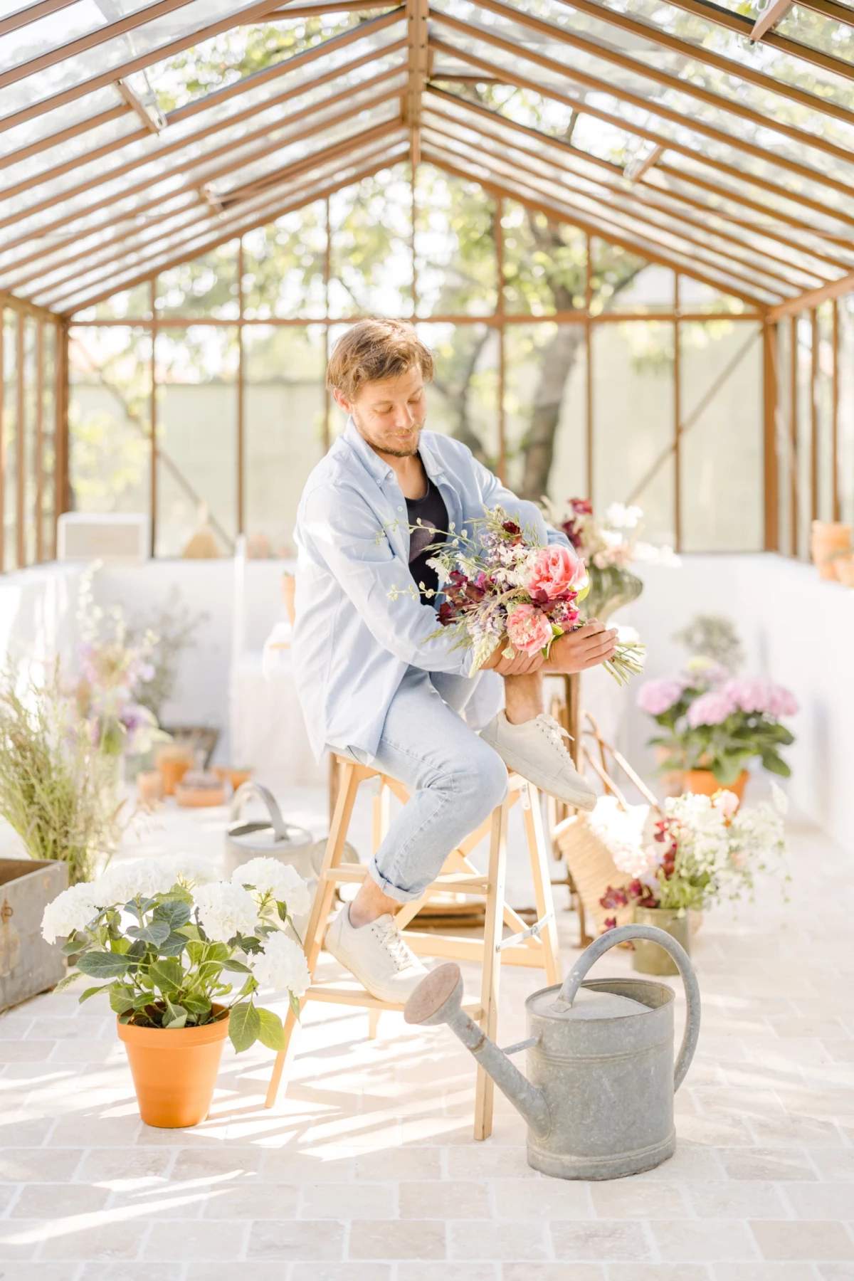 Séance photo corporate fleuriste : artisan créant un bouquet dans une verrière lumineuse, ambiance douce et naturelle en Vendée