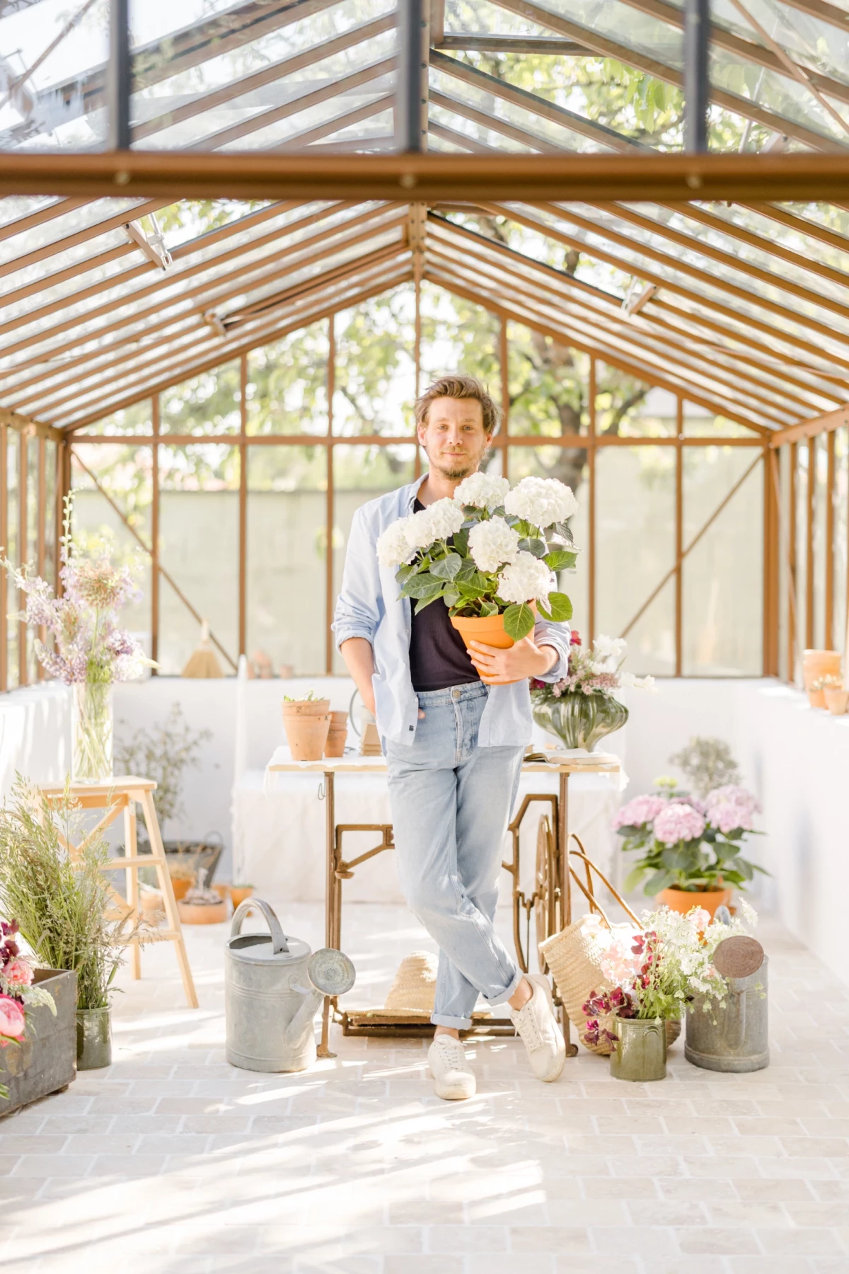 Portrait corporate fleuriste tenant bouquet de fleurs blanches dans verrière lumineuse, ambiance naturelle et professionnelle