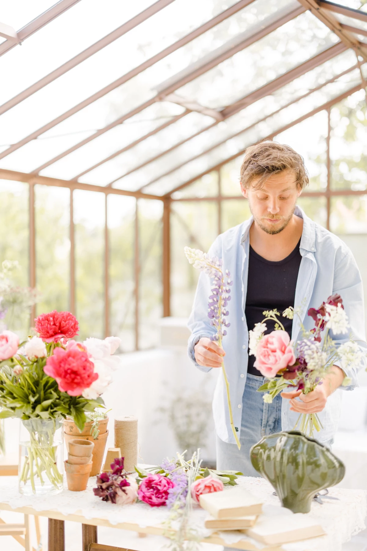Portrait corporate fleuriste en Vendée : artisan créant un bouquet dans une verrière lumineuse, ambiance douce et naturelle