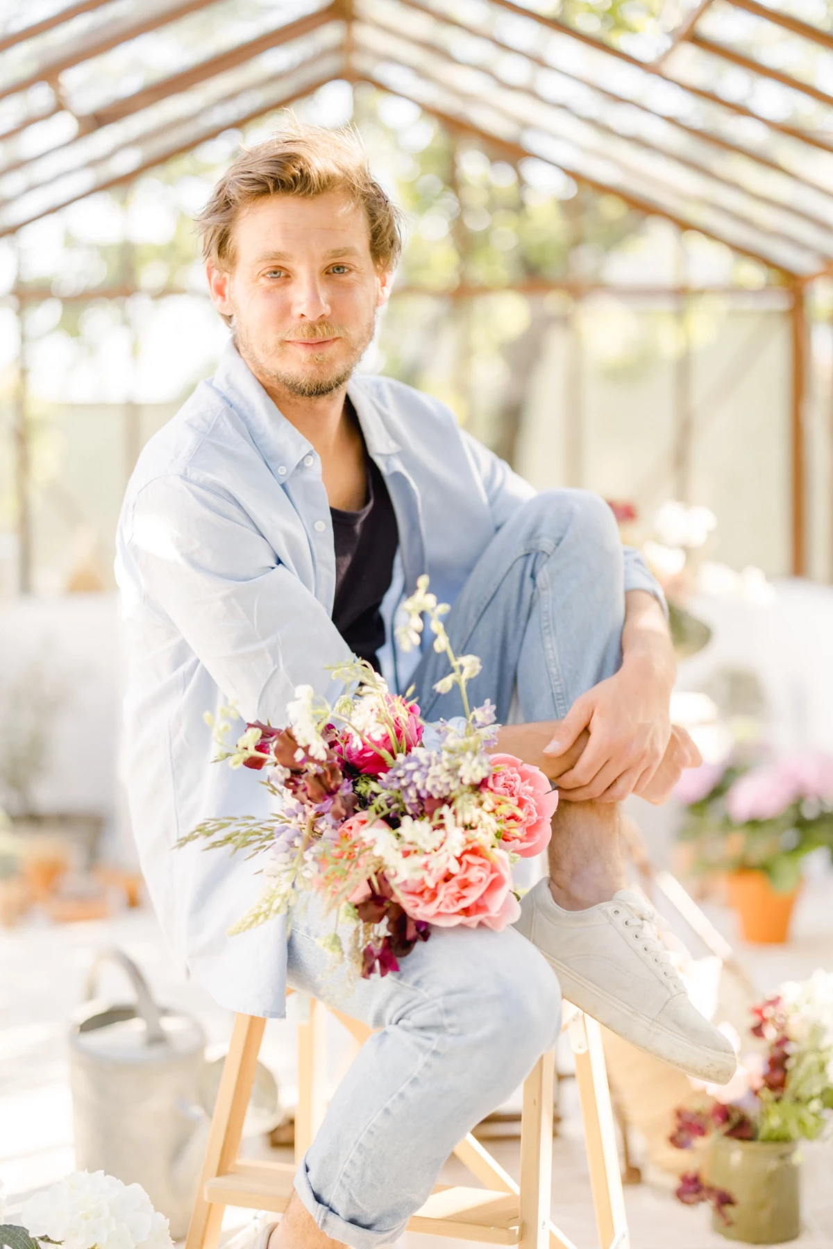 Portrait corporate fleuriste tenant un bouquet romantique sous verrière, lumière naturelle douce et univers floral délicat