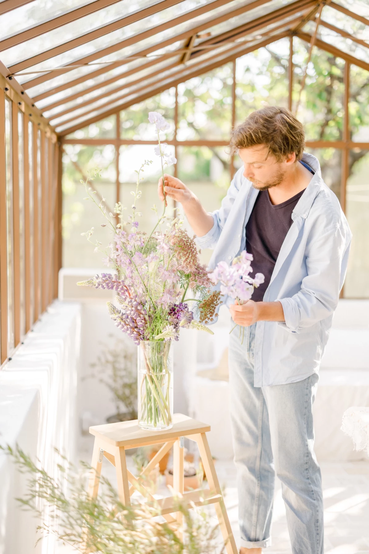 Portrait corporate d'un fleuriste arrangeant un bouquet de fleurs séchées dans une verrière lumineuse, ambiance douce et naturelle