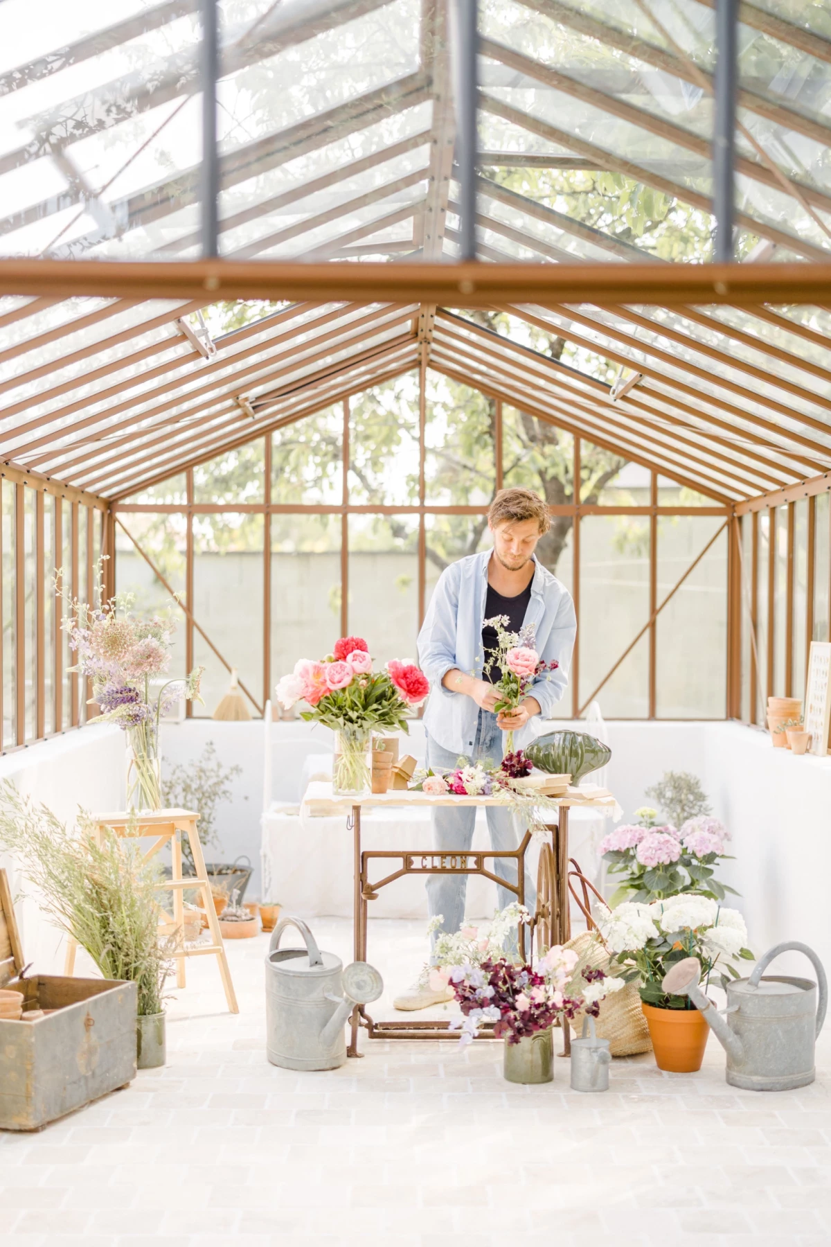 Portrait corporate fleuriste : artisan arrange des bouquets de fleurs dans une verrière lumineuse, ambiance douce et naturelle