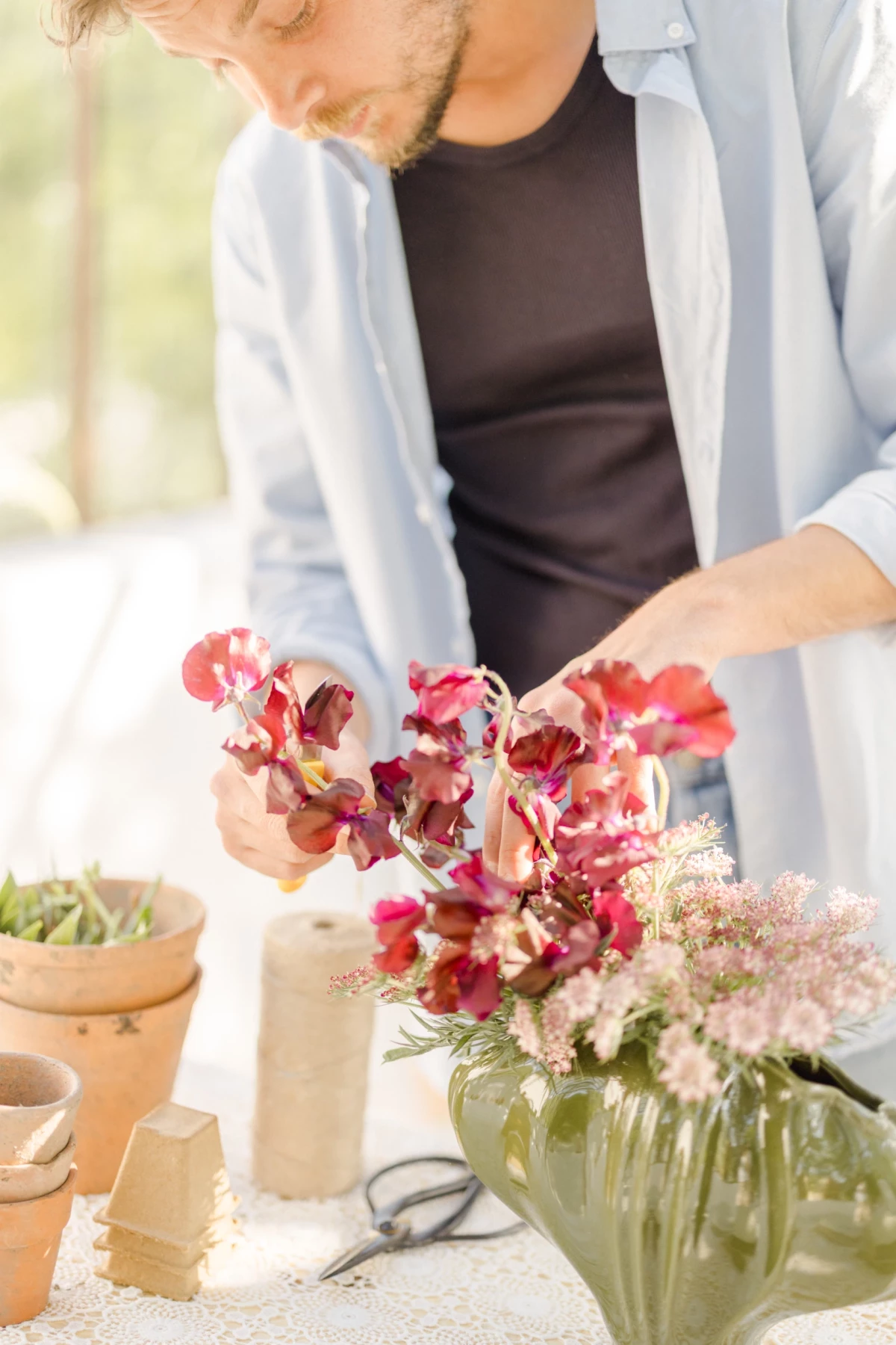 Portrait corporate fleuriste Vendée : mains délicates arrangeant un bouquet de fleurs rose et bordeaux dans une verrière lumineuse