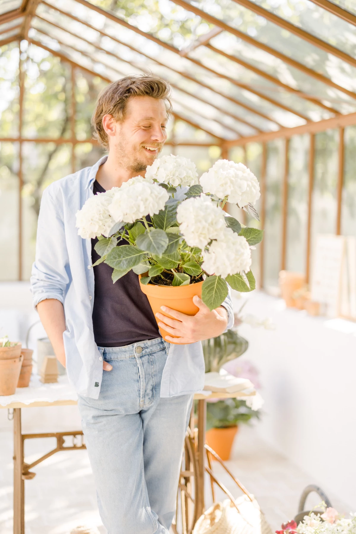 Portrait corporate fleuriste en verrière : artisan souriant avec bouquet de fleurs blanches, ambiance douce et lumineuse