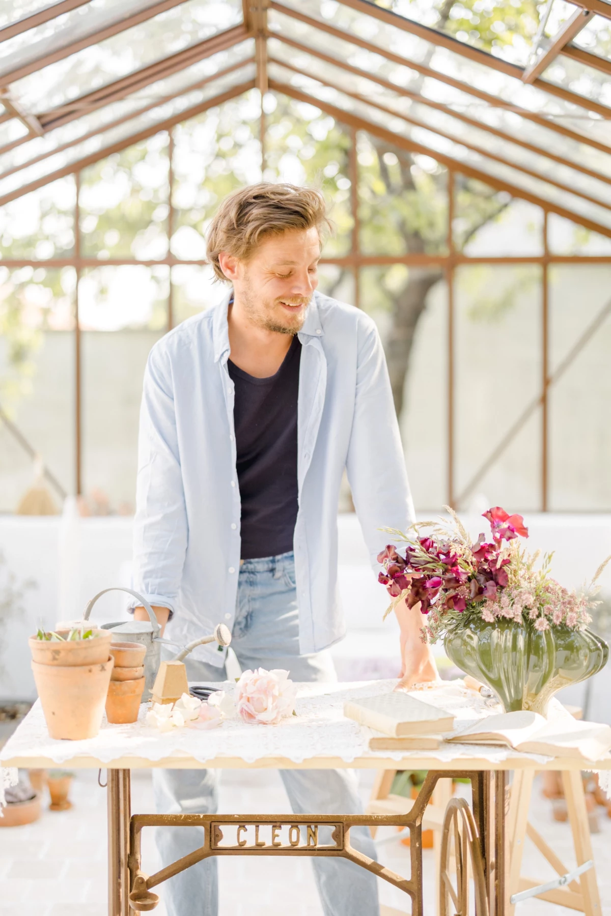 Portrait corporate d'un fleuriste dans sa verrière lumineuse, arrangeant des bouquets colorés avec un sourire naturel