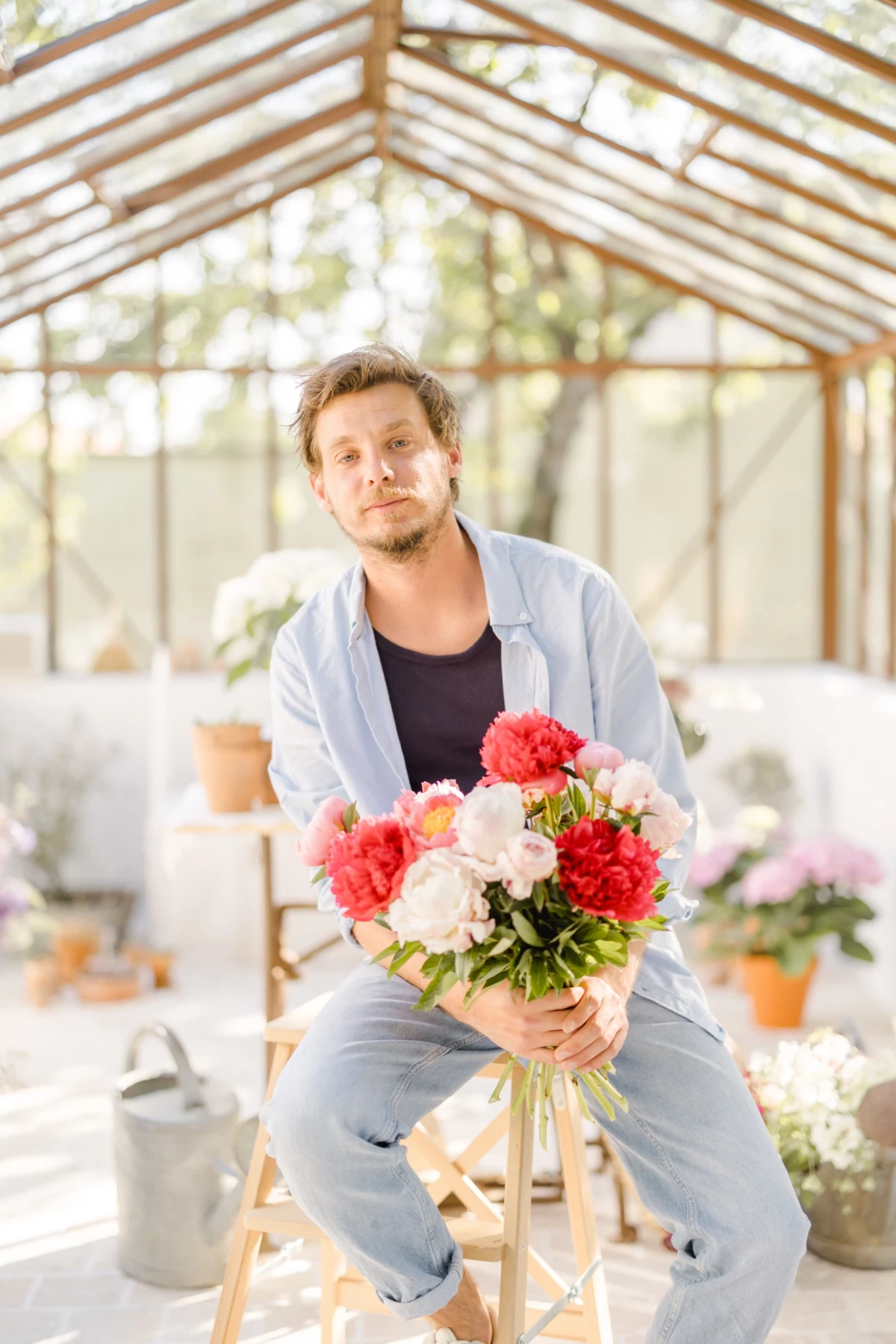 Portrait corporate d'un fleuriste assis avec un bouquet coloré dans sa verrière lumineuse, atmosphère douce et printanière