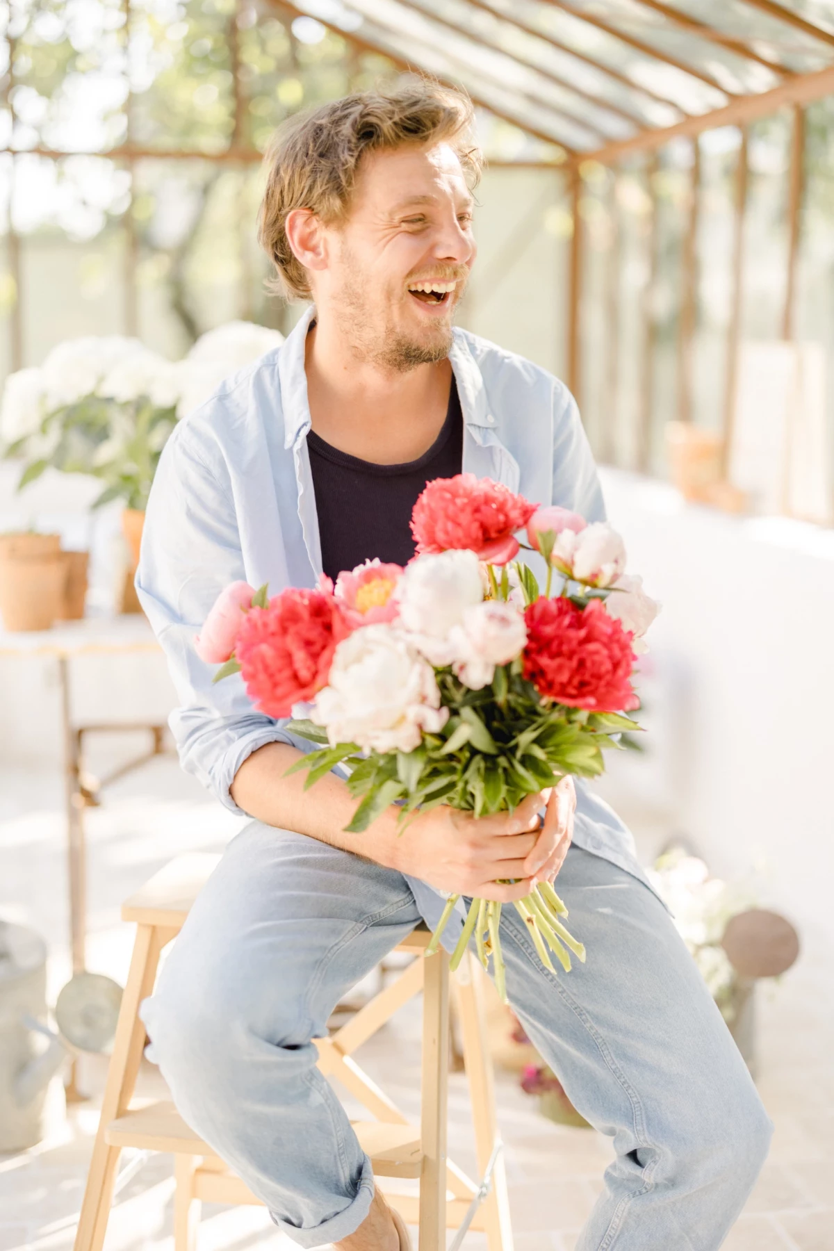 Portrait corporate fleuriste : artisan souriant présente un bouquet de pivoines roses et blanches dans une verrière lumineuse
