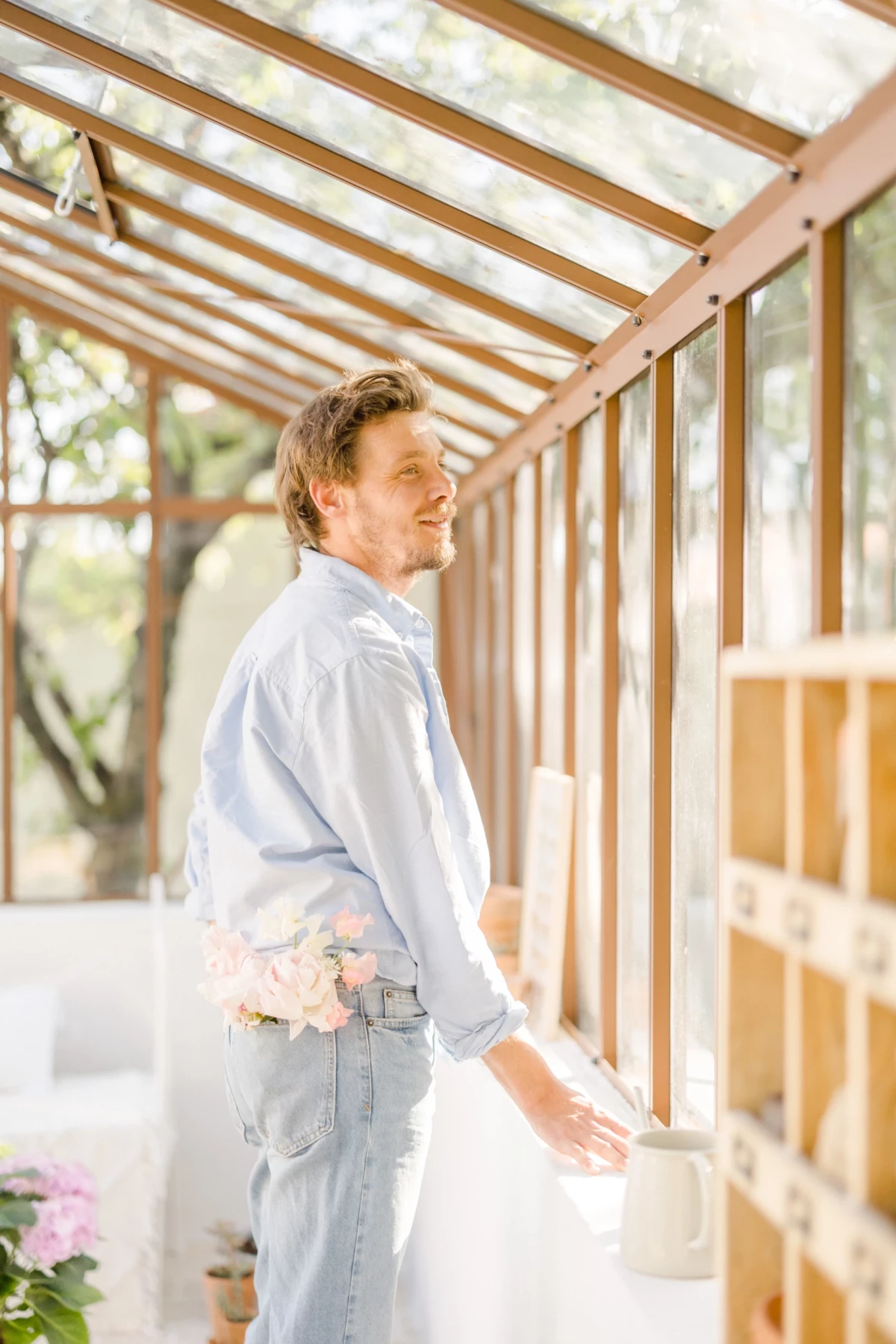 Portrait corporate d'un fleuriste artisan souriant dans sa verrière lumineuse, ambiance douce et naturelle en Vendée