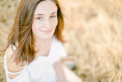 Portrait lumineux d'une jeune femme souriante dans un champ doré, vêtue d'un pull blanc