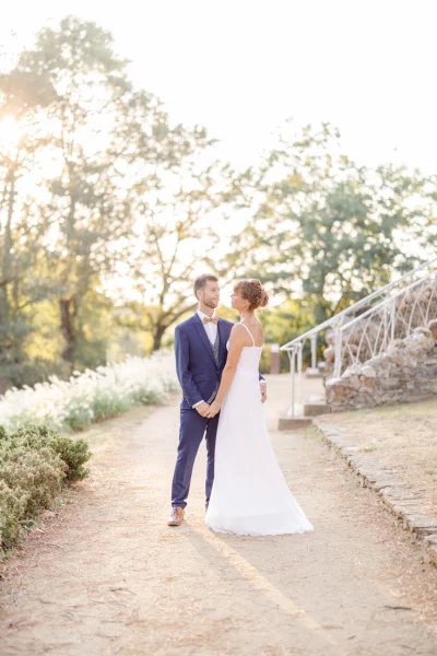 Couple de mariés marchant main dans la main sur un chemin de jardin au coucher du soleil