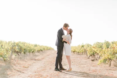 Couple de mariés s'embrassant tendrement au milieu des vignes sous un ciel lumineux