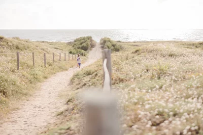 Enfant marchant sur un chemin côtier bordé de dunes sauvages menant vers l'océan