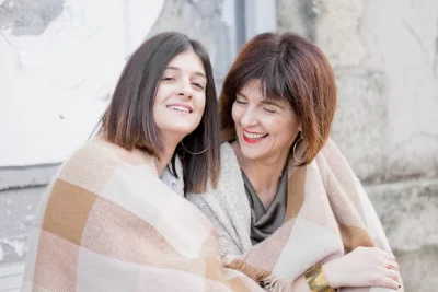 Mère et fille enlacées sous une couverture beige, partageant un moment de complicité joyeuse