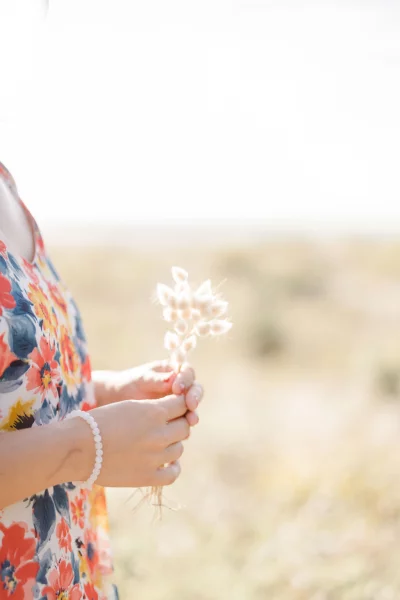 Petite fille tenant délicatement une fleur blanche séchée dans ses mains ornées d'un bracelet de perles