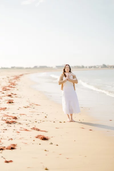 Femme en robe blanche marchant pieds nus sur une plage déserte au bord de l'océan