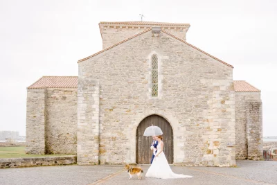Couple de mariés devant une église en pierre ancienne avec un chien, photographie de mariage élégante
