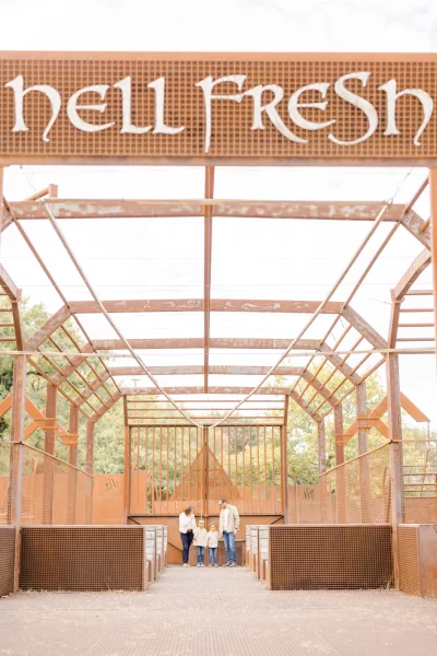 Trois enfants assis sur un banc sous une structure architecturale aérienne en bois au texte Hell Fresin